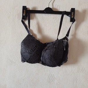 Svart spets-bh - Elegant svart bh med spetsdetaljer och justerbara axelband. Perfekt för en stilren look med en touch av lyx. Den har en klassisk design med hakknäppning bak.