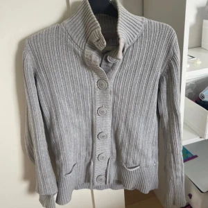 Grå ribbad kofta från H&M - en super cool kofta från hm i storlek M. Den har knappar hela vägen upp så man kan välja om man vill ha den öppen eller stängd. Har en polokrage och snören i midjan så man dra åt den, super fint skick
