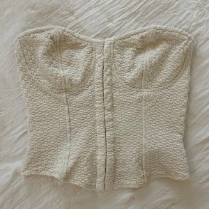 Beige korsettopp - En beige axelbandslös korsettopp son knäpps framtill med små hakar. 