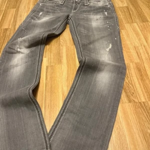 Grå jeans från Rock Revival - Snygga grå jeans från Rock Revival med slitna detaljer och broderade bakfickor. 