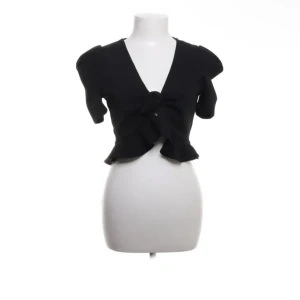 Svart bolerotopp från Fashion Nova - Snygg svart bolerotopp från Fashion Nova med korta ärmar och en knytning framtill. Toppen har en volangdetalj vid nederkanten som ger en extra touch. Perfekt för att lägga till en stilfull look till din outfit.