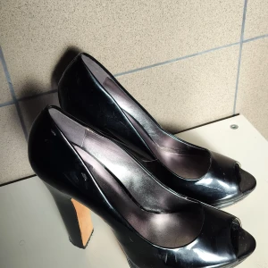 Svarta pumps från Calvin Klein - Snygga svarta pumps från Calvin Klein med öppen tå och hög klack. Perfekta för en elegant look. Tillverkade i ett glänsande material som ger en lyxig känsla.