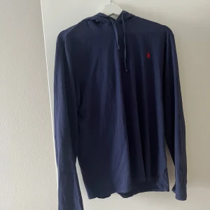 Mörkblå hoodie från Polo Ralph Lauren - Säljer en stilren mörkblå hoodie från Polo Ralph Lauren med en liten röd logga på bröstet. Tröjan har långa ärmar. Perfekt för en avslappnad look.