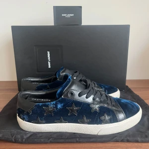 Extremt unika skor från Saint Laurent - Snygga blå dojor från Saint Laurent i sammet med stjärnmönster. Skorna har svarta detaljer och en vit sula. Perfekta för att ge din outfit en unik touch. Med blått mocka likt fluff runt skon. Riktigt feta!!!! PRIS KAN DISKUTERAS! Original storlek är 40 men passar större!