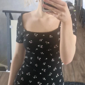 Svart blommig klänning - Säljer en söt svart klänning med små blommor i rosa och vitt. Klänningen har korta ärmar och en fin öppen rygg. Perfekt för en somrig look! 🌸