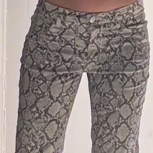 Ormmönstrade byxor - Snygga ormmönstrade byxor i grå och beige ton. Byxorna har en tight passform och är perfekta för att sticka ut. De har en klassisk dragkedja och knapp framtill.