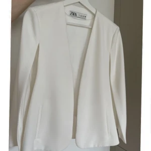 Vit kavaj/poncho från Zara - En poncho i kostym material, ärmarna är öppna. Slutsåld modell från Zara, stilren och i nyskick. Strl. S men passar även M