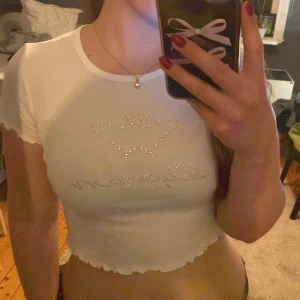 Vit croppad topp från Gina Tricot - Säljer en vit croppad topp från Gina Tricot med glittrande detaljer i form av en fjäril och texten 'Papillon'.