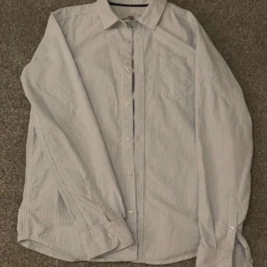 Randig skjorta från Hampton Republic - Säljer en stilren och klassisk randig skjorta från Hampton Republic. Skjortan är i en ljusblå och vit färgkombination med knappar framtill och en bröstficka. Perfekt för en avslappnad men ändå uppklädd look.