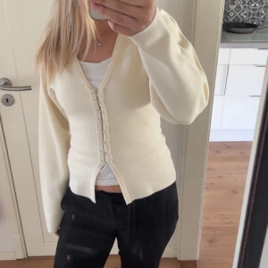 Beige kofta med knappar - Säljer en stilren beige kofta med knappar framtill. Koftan har en v-ringad design och långa ärmar, perfekt för en elegant look. Passar bra till både jeans och kjol. Säljer då den inte har kommit till någon användning💞