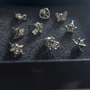 Set med silverfärgade örhängen - Säljer ett set med olika silverfärgade örhängen. Setet innehåller flera unika designer, inklusive hjärtan, fjärilar och stjärnor, alla dekorerade med glittriga stenar. Perfekt för att mixa och matcha efter humör och stil.