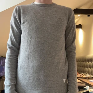 Grå tröja från Lindbergh - Säljer en stilren grå tröja från Lindbergh. Tröjan har en klassisk rund hals och långa ärmar, perfekt för en avslappnad look. Den är tillverkad i ett mjukt material som ger en bekväm passform. 