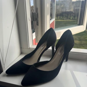 Svarta pumps med spetsig tå - Eleganta svarta pumps med spetsig tå och hög klack. Perfekta för en stilren look. Tillverkade i ett material som ger en lyxig känsla.