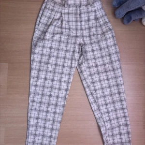 Rutig byxa från Monki - Snygga högmidjade byxor från Monki i ett klassiskt rutigt mönster. Byxorna har en rak passform och är perfekta för en stilren look. De är tillverkade i ett bekvämt material som passar bra för både vardag och mer uppklädda tillfällen.