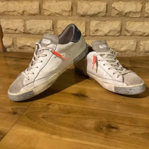 Vita sneakers från Philippe Model - Snygga vita sneakers från Philippe Model med grå detaljer och en orange accent på sidan. Skorna har snörning och en rund tå. Pris kan diskuteras 