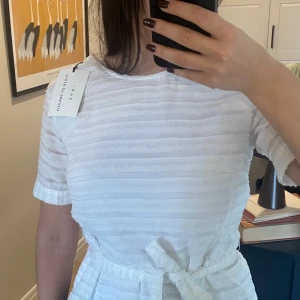 Vit blus från Tiger of Sweden - Säljer en elegant vit blus från Tiger of Sweden med subtila ränder och knytband i midjan. Helt ny med prislapp. Ordinarie pris 1699 kr.