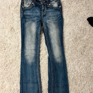 Miss Me jeans med broderade bakfickor - Snygga lågmidjade bootcut jeans från Miss Me med unika broderade detaljer på bakfickorna i storlek 26! Aldrig använda, original pris: 1260kr. Midjemått: 36cm, innerbenslängd: 78cm, grenen: 19cm. För referens är jag 167cm. Priset kan diskuteras!