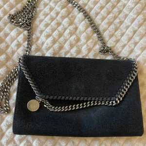 Stella mccartney falabella wallet crossbody bag - Snygg svart axelväska med kedjedetaljer och en stilren design. Väskan har en kedja som axelrem och en magnetisk stängning. Perfekt för att ge en edgy touch till din outfit. Köpt för 6920 kr🤍