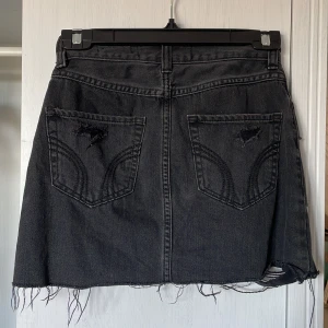 Svart jeanskjol från Hollister - Snygg svart jeanskjol från Hollister med slitna detaljer och fransig nederkant. Kjolen har en klassisk femficksdesign och medel hög midja men den kan bäras hur man vill,jag själv har haft den som lågmidjad då kjolen är kort  