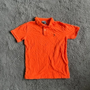 Ralph Lauren piké  - Snygg orange pikétröja från Polo Ralph Lauren i storlek L. Klassisk krage med två knappar och den ikoniska broderade loggan på bröstet. Tillverkad i 100% bomull, perfekt för dig som gillar stilren och sportig look. Passar dig som vill sticka ut med färg. Storlek L 14-16 år men bör sitta som XS