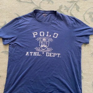 Blå t-shirt från Polo Ralph Lauren - Snygg blå t-shirt från Polo Ralph Lauren med vit tryckt logga och text på bröstet. Perfekt till skolstart. Pris kan diskuteras