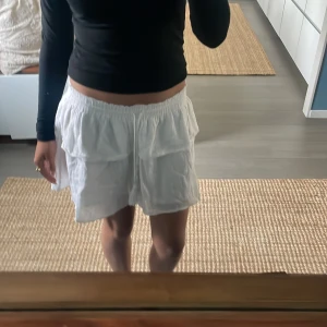 Vit kortkjol med volanger - Supersöt vit kortkjol med volangdetaljer och resår i midjan. Kjolen har en luftig och lätt känsla, perfekt för varma dagar. Passar dig som gillar en avslappnad och feminin stil.