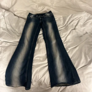 Bootcut jeans från Cheap Monday - Säljer ett par snygga bootcut jeans från Cheap Monday i mörkblå tvätt med ljusa slitningar. Jeansen har klassisk femficksdesign, normal passform och är tillverkade i jeansmaterial med stretch. Perfekt för dig som gillar retrovibbar och vill sticka ut med breda ben. W 23 