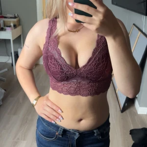 Lila spetsig topp - Superfin lila bralette topp med bred spets och djup v-ringning. Den är croppad och har ett snyggt spetsmönster över hela toppen. Perfekt att styla med jeans eller under en skjorta för en cool look.