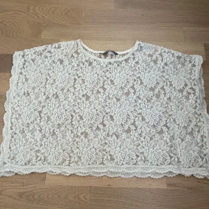 Vit spetsblus med blommönster från Lindex  - Säljer en vit blus i spets med blommigt mönster och rund hals. Blusen är croppad och har korta, vida ärmar. Spetsen är detaljerad och ger en romantisk vibe. Perfekt att ha över ett linne eller bandeau. Supersnygg till svarta jeans eller kjol!