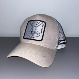 Beige Bugs Bunny keps från Capslab - Snygg beige keps med grått mesh-tyg baktill och en stor Bugs Bunny-patch framtill. Justerbar snapback och coolt Capslab-märke på sidan. 