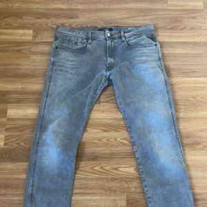 Replay grå jeans med broderade fickor - Snygga grå jeans från Replay med coola broderade detaljer på bakfickorna. Jeansen har klassisk femficksdesign, knappgylf och en tvättad look som ger en avslappnad vibe. Passar dig som gillar streetstyle och vill ha ett par jeans med unik touch.