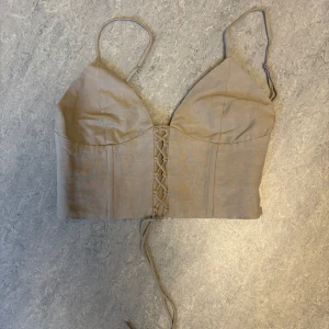 Beige korsett-topp med snörning XS - Snygg beige korsett-topp med smala justerbara axelband och snörning framtill. Toppen har en croppad passform och är trendig. Pris kan diskuteras