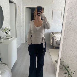Beige omlottop från 157 Lilja - Säljer en beige omlottop från 157, modell Lilja. Toppen har lång ärm, v-ringning och knyt i midjan som ger en snygg siluett. Materialet är mjukt och lätt, perfekt för layering. Passar dig som gillar stilrena och enkla plagg med twist.