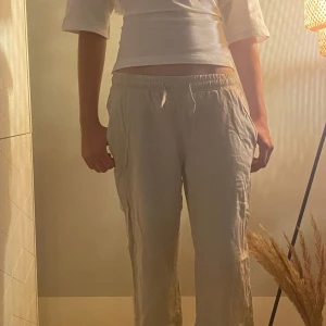 Beiga linnebyxor med snörning - Säljer ett par chill beiga linnebyxor med elastisk midja och snörning framtill. Byxorna har en loose passform och raka ben, perfekta för varma dagar. Materialet är linne som ger en skön och luftig känsla. Passar dig som gillar avslappnad stil.