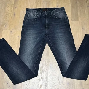 Mörkblå Nudie Jeans straight fit - Snygga mörkblå jeans från Nudie Jeans med klassisk femficksdesign och subtila slitningar framtill. Modellen har raka ben och normal passform, perfekt för dig som gillar en clean och tidlös look. Jeansen är tillverkade i slitstark bomull och har silverfärgade detaljer. W27 L32
