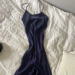 Marinblå långklänning med smala axelband - Elegant marinblå långklänning med smala axelband och figurnära passform. Klänningen har en slät, lätt glansig yta och faller snyggt längs kroppen. Axelbanden går att justera! Perfekt för bröllop, bal, fest! 😌
