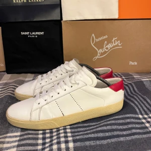 Saint Laurent Skor - Tha nu säljer jag mina snygga vita sneakers från Saint Laurent med röd detalj på hälen. Skorna är i skinn och har en beige sula med retrovibbar. Perfekta för dig som gillar stilrena och exklusiva sneakers med en twist. Skorna är i helt okej med sina skavanker men skickat får ni avgöra själva. Jag tar jättegärna byten och prisförslag. Med vänliga hälsningar Oscar