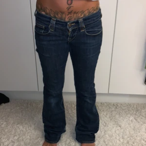 Blå bootcut jeans från Replay - Snygga mörkblå jeans från Replay med bootcut passform och klassiska detaljer. Jeansen har kontrastsömmar, fem fickor och coola dragkedjor på bakfickorna. Materialet är slitstarkt jeans och midjan är låg. Perfekt för dig som gillar en avslappnad stil.