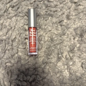 Meet Matt(e) Hughes flytande läppstift - Säljer ett Meet Matt(e) Hughes flytande läppstift från theBalm i färgen 'Honest', en snygg varm nude-rosa ton. Kommer i en smidig tub med silverfärgat lock och transparent plastförpackning. Perfekt för dig som gillar matta läppar med lång hållbarhet.