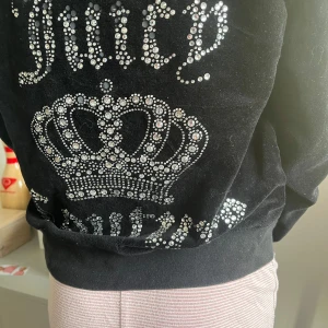 Juicy flis  - Svart velourjacka från Juicy Couture med glittrande strassdetaljer och krona på ryggen. Jackan har dragkedja framtill, huva och två fickor. Det är äkta juicy men några av ”pärlorna har försvunnit men det är inget man tänker på ! 🤗 det är storlek M men jag tycker att den uppfattas som xs/xxs😅🌷