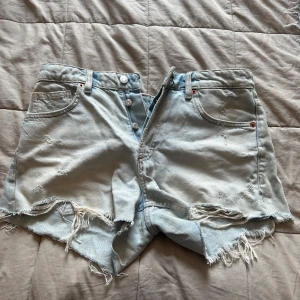 Ljusblå jeansshorts med fransar/slitningar - Säljer ljusblå jeansshorts midrise från zara. De är knappt använda men köpta med slitningar/ fransar. Storlek 38