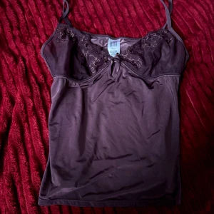Lila linnetopp med broderad spets - Snygg lila linnetopp med tunna axelband och broderad spets upptill. Toppen har en liten öppning framtill och är gjord i ett mjukt, glansigt material som känns lyxigt mot huden. Perfekt för dig som gillar detaljer och vill ha en feminin look.🐆🐆Ej använd. 