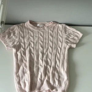 Ljusrosa stickad tröja Gina Tricot - Supersöt ljusrosa stickad tröja från Gina Tricot med korta ärmar och snyggt flätmönster. Rund halsringning och ribbade muddar ger en chill vibe. Perfekt att styla med jeans eller kjol för en fräsch look.