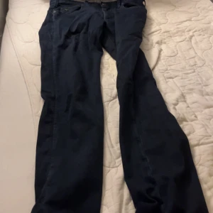 Emporio Armani mörkblå jeansbyxor - Snygga mörkblå jeansbyxor från Emporio Armani med klassisk femficksdesign och silverfärgade logodetaljer både fram och bak. Byxorna har rak passform och är tillverkade i mjukt bomullsmaterial med en hint av stretch för extra komfort. Perfekt för dig som gillar stilrena och exklusiva jeans. Passar dig som är ca 180-188cm lång. Denna modell säljs inte längre och kostade mig 1800 kr när jag köpte den 