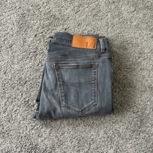 Slim grå jeans från Tiger of Sweden , 33/34 - Slimmade grå jeans från T/J, tillverkade i Italien. Klassisk femficksmodell med snygga kontrastsömmar och läderpatch bak i midjan. Jeansen har en smal passform och är perfekta för dig som gillar stilrena och moderna jeans.