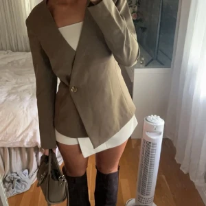 Beige kavaj från NA-KD med knapp - Snygg beige kavaj från NA-KD med en stilren omlott-design och guldfärgad knapp framtill. 