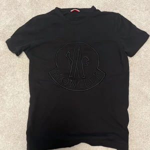 Svart t-shirt från Moncler - Snygg svart t-shirt från Moncler med ett stort, diskret logotryck på framsidan. Perfekt för en stilren look. Tillverkad i mjukt material för extra komfort.