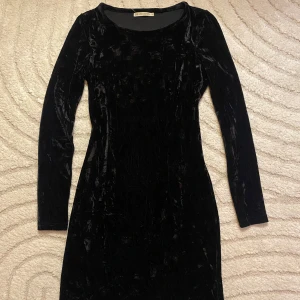 Svart sammetklänning Brave Soul XS - Supersnygg svart klänning från Brave Soul i mjuk sammet. Den har lång ärm, rund hals och en tight passform. Perfekt för dig som gillar en stilren look med lite lyxig känsla.