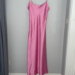 Rosa långklänning från Kappahl XS - Supersnygg rosa långklänning från Kappahl i storlek XS. (Oanvänd med prislapp) Klänningen har tunna axelband och är tillverkad i ett glansigt satinliknande material som ger en lyxig känsla. Den har en enkel, rak passform och är perfekt för dig som vill sticka ut med färg. 