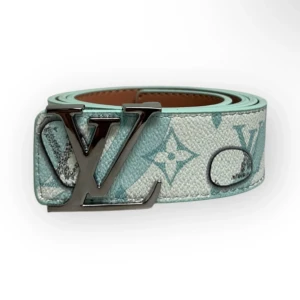 Louis Vuitton ljusblå bälte - Snyggt bälte från Louis Vuitton i ljusblått med klassiskt monogrammönster och stor LV-spänne i silver. Bältet har en stilren och modern look, perfekt för att lyfta din outfit. Materialet är exklusivt skinn med präglad yta och detaljer i silver.